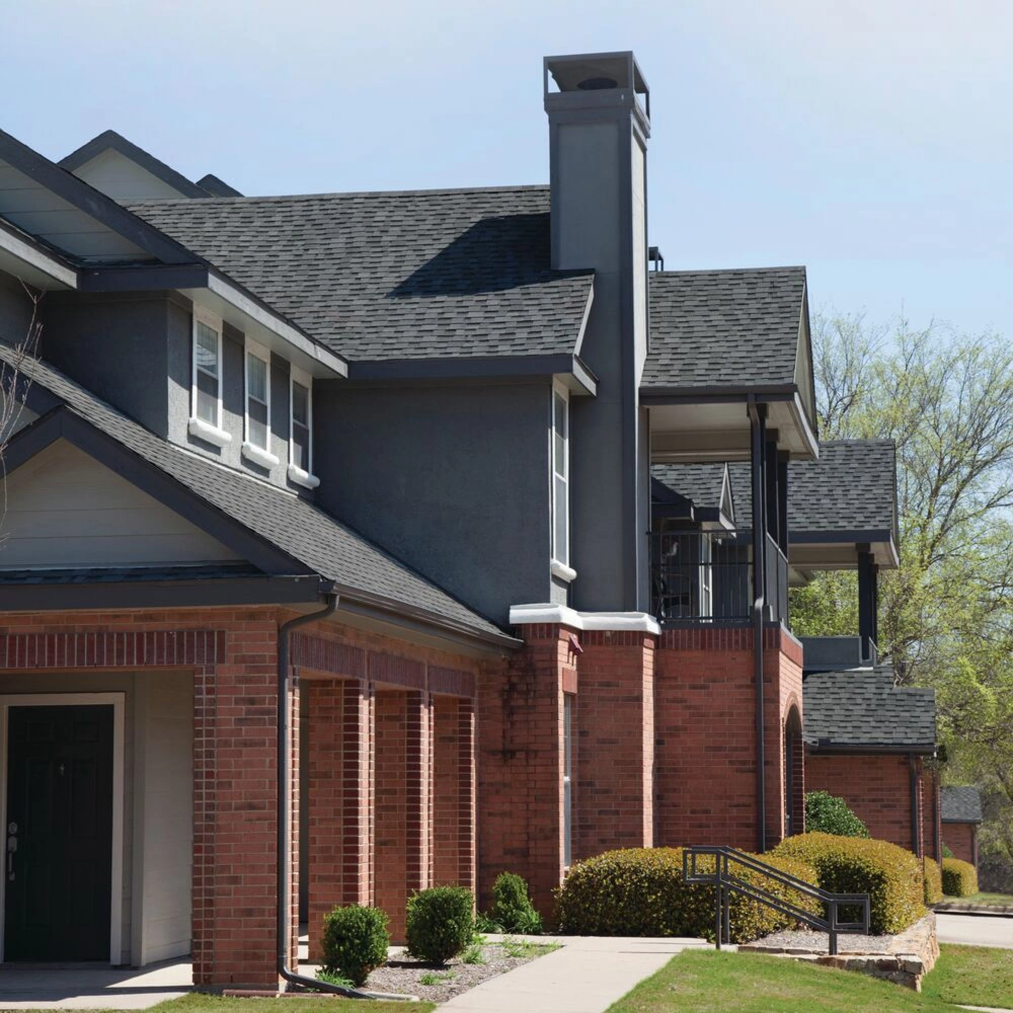 Front view of a modern house in Cambridge with a brick facade, dark shingle roof, and a small porch. Shrubs and a concrete path create an inviting entrance.