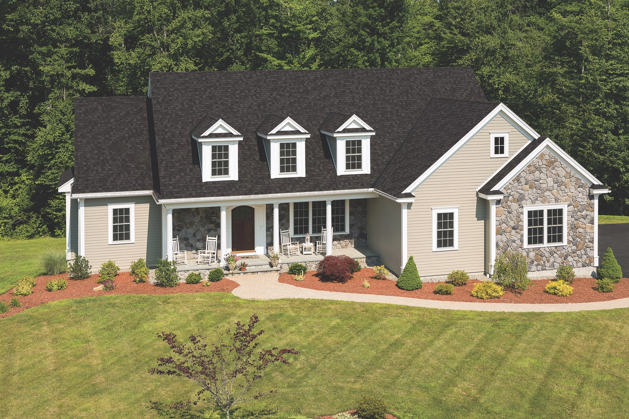 Front view of a modern house in Cambridge with a brick facade, dark shingle roof, and a small porch. Shrubs and a concrete path create an inviting entrance.