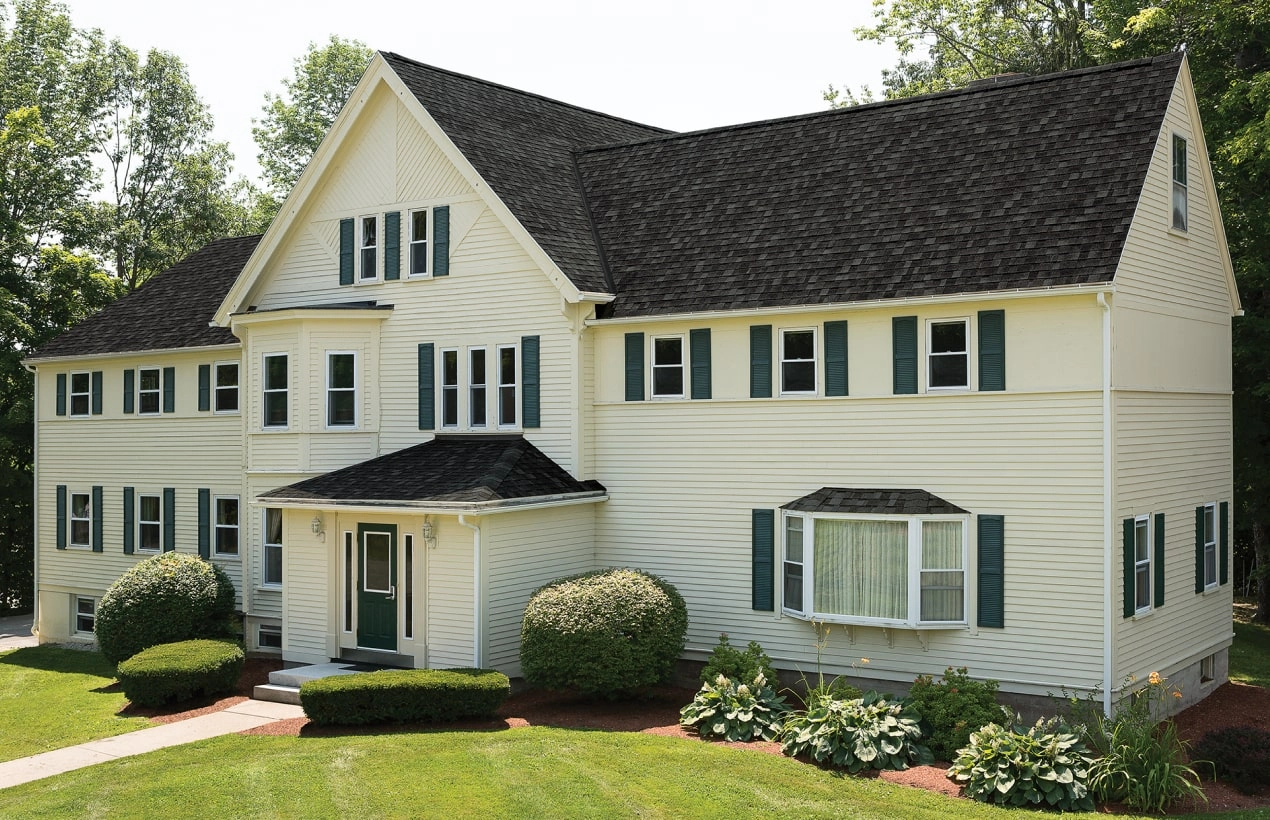 Front view of a modern house in Cambridge with a brick facade, dark shingle roof, and a small porch. Shrubs and a concrete path create an inviting entrance.