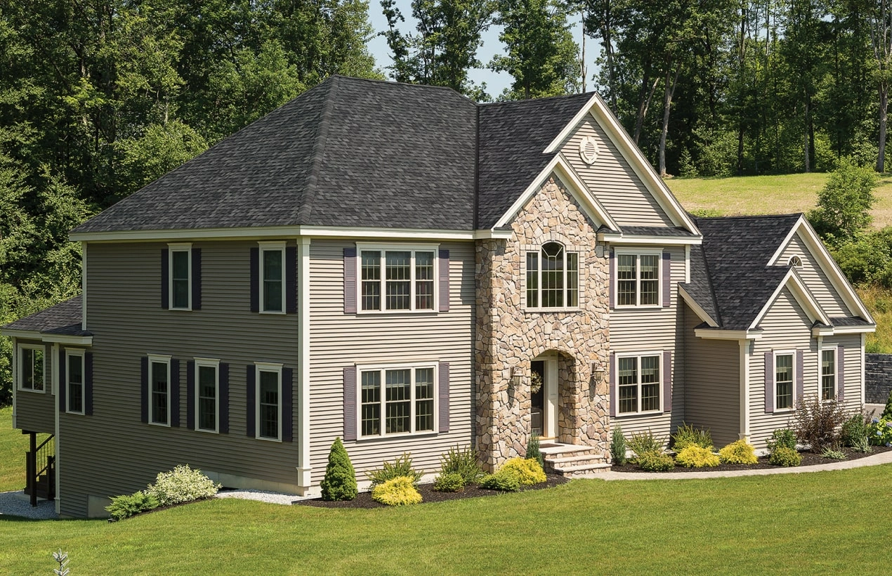 Front view of a modern house in Cambridge with a brick facade, dark shingle roof, and a small porch. Shrubs and a concrete path create an inviting entrance.