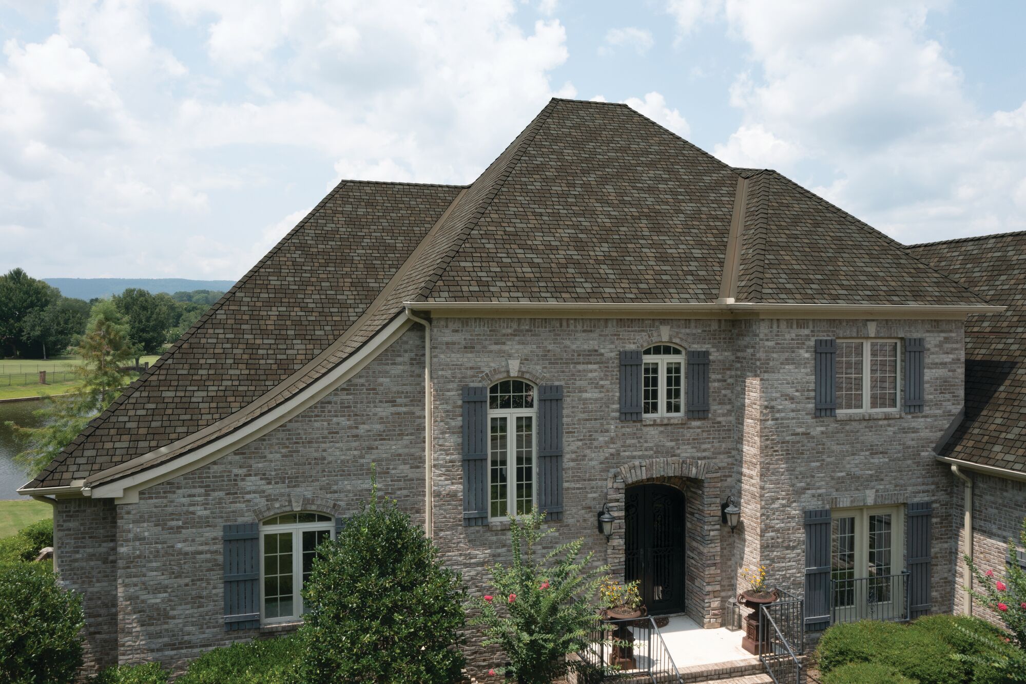 This elegant real estate gem features a large brick house with a steep, gabled roof, arched windows, and a central entrance, all nestled amidst lush greenery and trees.