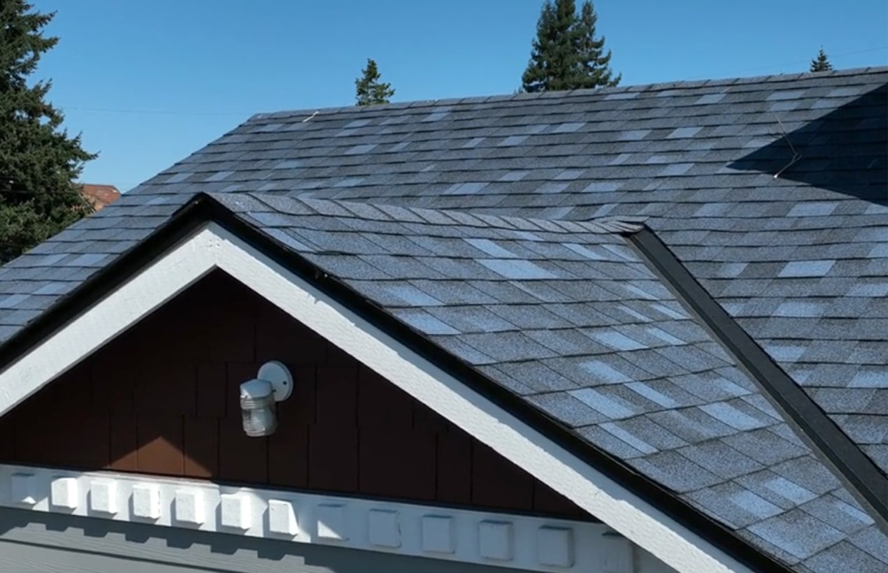 A gray shingled roof with a triangular gable and an exterior light fixture stands proudly. Trees are visible in the background against an Atlantic Blue sky, creating a serene dynasty of nature and architecture.